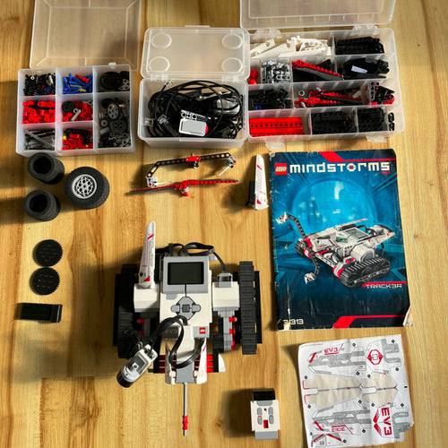 Robotic components and parts on a wooden surface with a Mindstorms Track3r build instruction booklet
